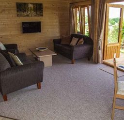 A living room with two dark sofas a coffee table a wall-mounted TV and open double doors leading outside at Pennylands Willow Lodge in Broadway