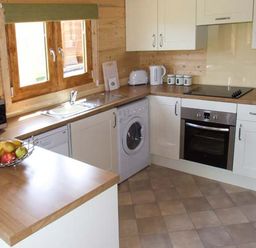 A kitchen with white cabinets wood countertops a window a sink an oven a washing machine and a fruit bowl at Pennylands Willow Lodge Broadway