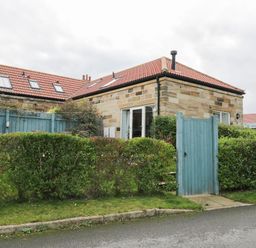 A corner stone house with a red tiled roof and blue wooden fence with green hedges at Mallard Cottage in Whitby