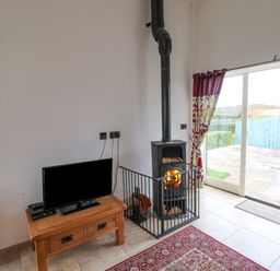 A small television on a wooden table beside a wood stove with a fire inside and a rug on the floor at Mallard Cottage in Whitby