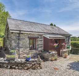 A stone cottage with flower pots on a low wall and a gravel pathway at Bwythyn Y Wennol in Nantmor near Beddgelert 