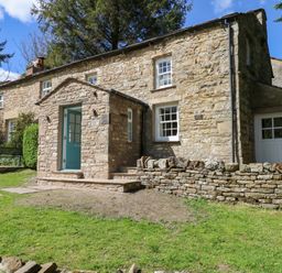 A stone house with a blue door and steps surrounded by grass and trees at Farrier's Cottage in Garsdale