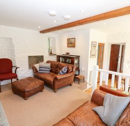 A living room with leather sofas, a red armchair, wooden furniture, and stone walls at Farrier's Cottage in Garsdale