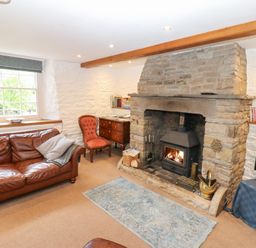 A living room with a stone fireplace a leather sofa an armchair a wooden chest a television and a window at Farrier's Cottage in Garsdale