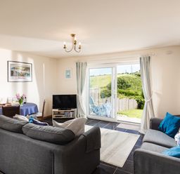 A living room with two gray sofas a dining table with chairs a TV and sliding glass doors leading outside at Nectan in Mevagissey