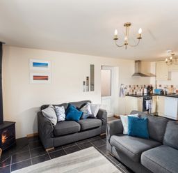 A living room with two gray sofas a wood stove and an adjoining kitchen at Nectan in Mevagissey