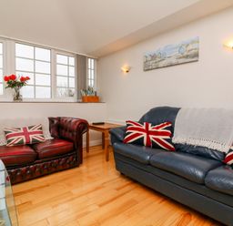 A living room with two leather sofas with union jack pillows and a wooden floor at The Well House Apartment in Watchet