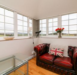A sitting area with a red leather sofa a pillow with a union jack a glass table and large windows at The Well House Apartment in Watchet