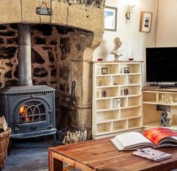 A room with a wood burning stove in a stone fireplace wooden coffee table with an open book shelving unit and a television at Bastle House in Haltwhistle near Hadrians Wall