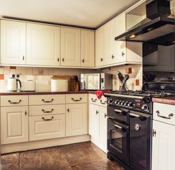 A kitchen with cream cabinets a black stove and oven a microwave and countertop appliances at Bastle House in Haltwhistle near Hadrians Wall