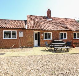 A brick house with a tiled roof and a patio area with a table and chairs at Hadleigh Farm Cottage in Gayton