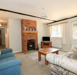 A living room with a brick fireplace two sofas a wooden coffee table and a TV at Hadleigh Farm Cottage in Gayton