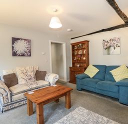 A living room with a patterned sofa, a blue sofa with yellow cushions, a wooden coffee table, a wooden cabinet with decorative plates, and floral paintings at Hadleigh Farm Cottage in Gayton
