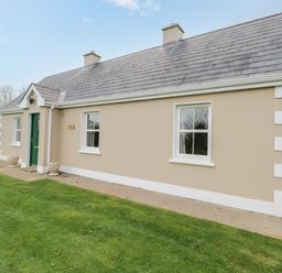 A beige house with a green door and white-framed windows on a grassy lawn at Tieve Baun in Ballintrillick near Kinlough County Sligo
