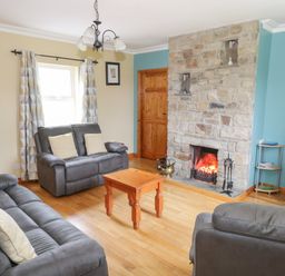 A living room with gray sofas a wooden coffee table a stone fireplace and a television at Tieve Baun in Ballintrillick near Kinlough County Sligo