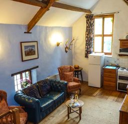 A living area with leather and upholstered chairs a small round table with wine glasses a kitchen with white refrigerator stove and wooden cabinets at The Mill in Bicknoller