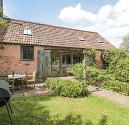 A garden with a grass lawn a barbecue a table and chairs outside a stone barn with wooden shutters at The Barn in Bicknoller