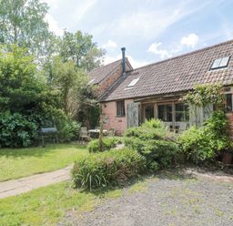 A garden with outdoor table and chairs near a stone house with tiled roof at The Barn in Bicknoller