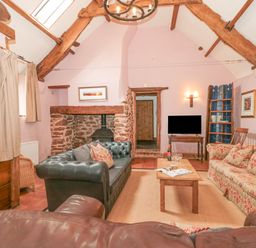 A living room with exposed wooden beams a stone fireplace two sofas a wooden coffee table and a television at The Barn in Bicknoller