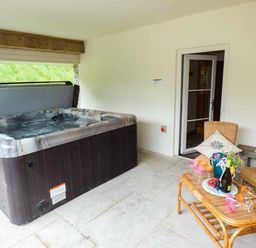 A covered patio with a hot tub and wicker furniture with drinks and flowers at The Old Mill in Dolau near Llandrindod Wells