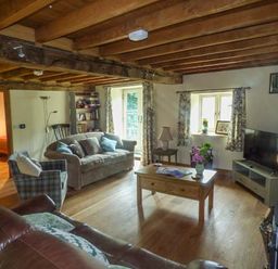 A living room with wooden ceiling beams a sofa armchair coffee table and a television at The Old Mill in Dolau near Llandrindod Wells