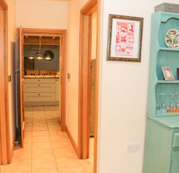 A hallway with wooden door frames leading to a kitchen with pendant lights and a turquoise cabinet with glasses and decor at The Old Mill in Dolau near Llandrindod Wells