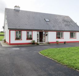A white house with red trim surrounded by grass and a paved driveway at Lough Mask Road Fishing Lodge in Ballinrobe County Mayo