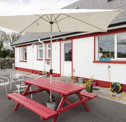 An outdoor patio with a red picnic table and white umbrella next to a white building with red trim and metal chairs at Lough Mask Road Fishing Lodge Ballinrobe County Mayo