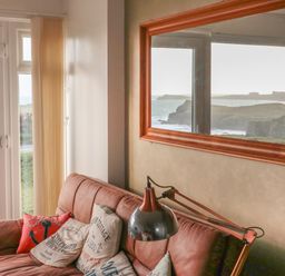 A living room with a sofa near a window showing a coastal view at Spindrift in Porth near Newquay
