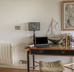 A desk with a laptop lamp decorative boat books and a mug with a stool in front at Spindrift in Porth near Newquay