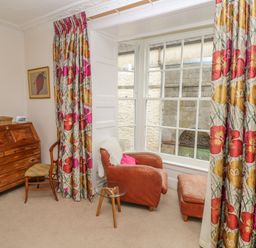 A corner of a room with a wooden desk chair and armchair beside large windows with floral curtains at Berlin House in Tenby