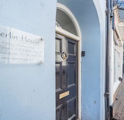 The entrance door of Berlin House holiday accommodation on a street with neighboring shops in Tenby