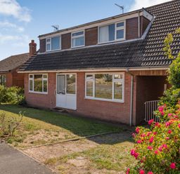 A house with a tiled roof and white framed windows and door with flowering bushes in a front garden at 38 Dale End in Brancaster Staithe near Burnham Market