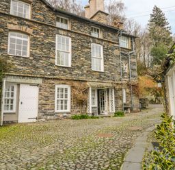 A stone building with white framed windows and doors on a cobblestone path surrounded by greenery at The Old Laundry in Clappersgate near Ambleside