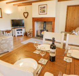 A dining table set with plates glasses and a bottle of wine in a living room with sofas a fireplace and a television at The Barn Cottage Steel near Hexham
