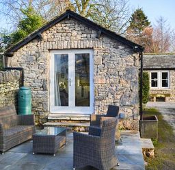 A stone cottage with glass doors and outdoor wicker furniture on a stone patio at The Potting Shed in Burton-in-Kendal near Kirkby Lonsdale