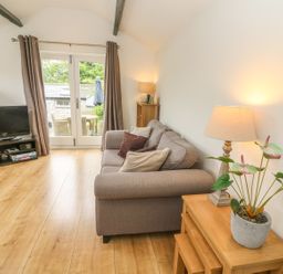 A living room with a sofa, wooden tables, a lamp, a television, and glass doors leading outside at The Potting Shed in Burton-in-Kendal near Kirkby Lonsdale