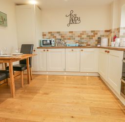 A kitchen with white cabinets wooden flooring a dining table with black chairs and kitchen appliances at Snowdrop Cottage in Aldingham