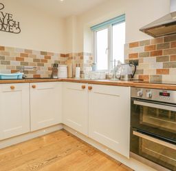 A kitchen with cream cabinets wooden countertops tiled backsplash and stainless steel oven at Snowdrop Cottage in Aldingham