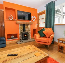 A living room with an orange wall a fireplace and a mounted television at Bluebell Cottage in Aldingham
