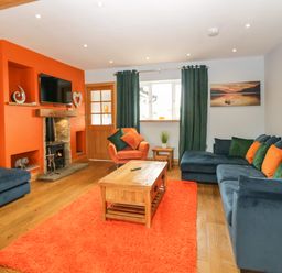 A living room with an orange wall fireplace wooden coffee table blue sofa and green curtains at Bluebell Cottage in Aldingham