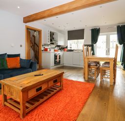 An open living room and kitchen with a wooden dining table and chairs a wooden coffee table and a blue sofa with cushions at Bluebell Cottage in Aldingham