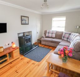 A living room with a sectional sofa and wooden coffee table with flowers a wood stove and a wooden media unit at Teach Teolai in Carraroe County Galway
