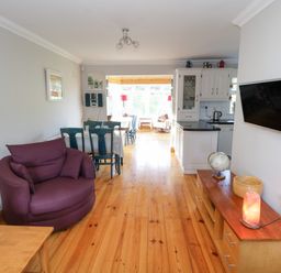A living area with a purple armchair a dining table and chairs a wooden floor and a mounted TV at Teach Teolai in Carraroe County Galway
