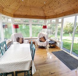 A conservatory with a wooden ceiling a table with chairs two armchairs with footstools and red floor lamps at Teach Teolai in Carraroe County Galway