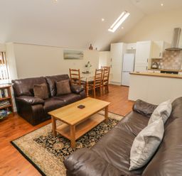 An open living room and kitchen with two leather sofas a wooden coffee table a dining table with chairs and kitchen cabinets at Hendoll Cottage 2 Fairbourne near Dolgellau