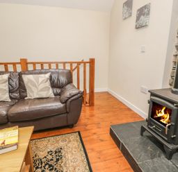 A living room with a leather sofa two pillows a coffee table with a book a rug and a wood burning stove at Hendoll Cottage 2 in Fairbourne near Dolgellau