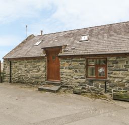 The exterior of a stone cottage with a wooden door and windows with flower planters outside at Hendoll Cottage 2 in Fairbourne near Dolgellau