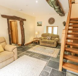 A living room with beige armchairs wooden staircase and stone floor at Hendoll Barn Friog near Fairbourne