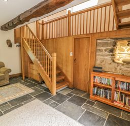 A sitting area with a sofa, staircase, bookshelf, and stone wall at Hendoll Barn in Friog near Fairbourne